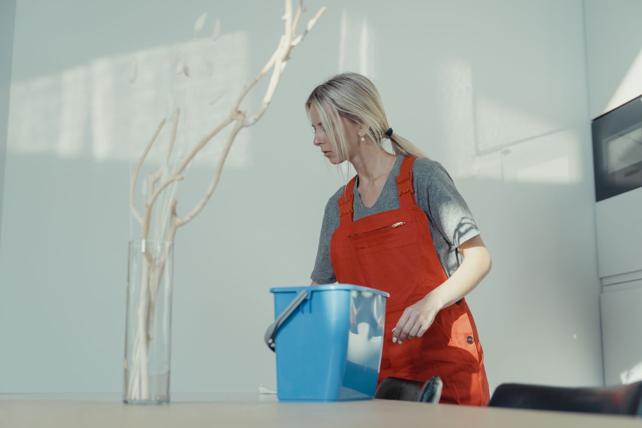 services-02 A woman in a red uniform cleans indoors with a blue bucket, ensuring a spotless environment.