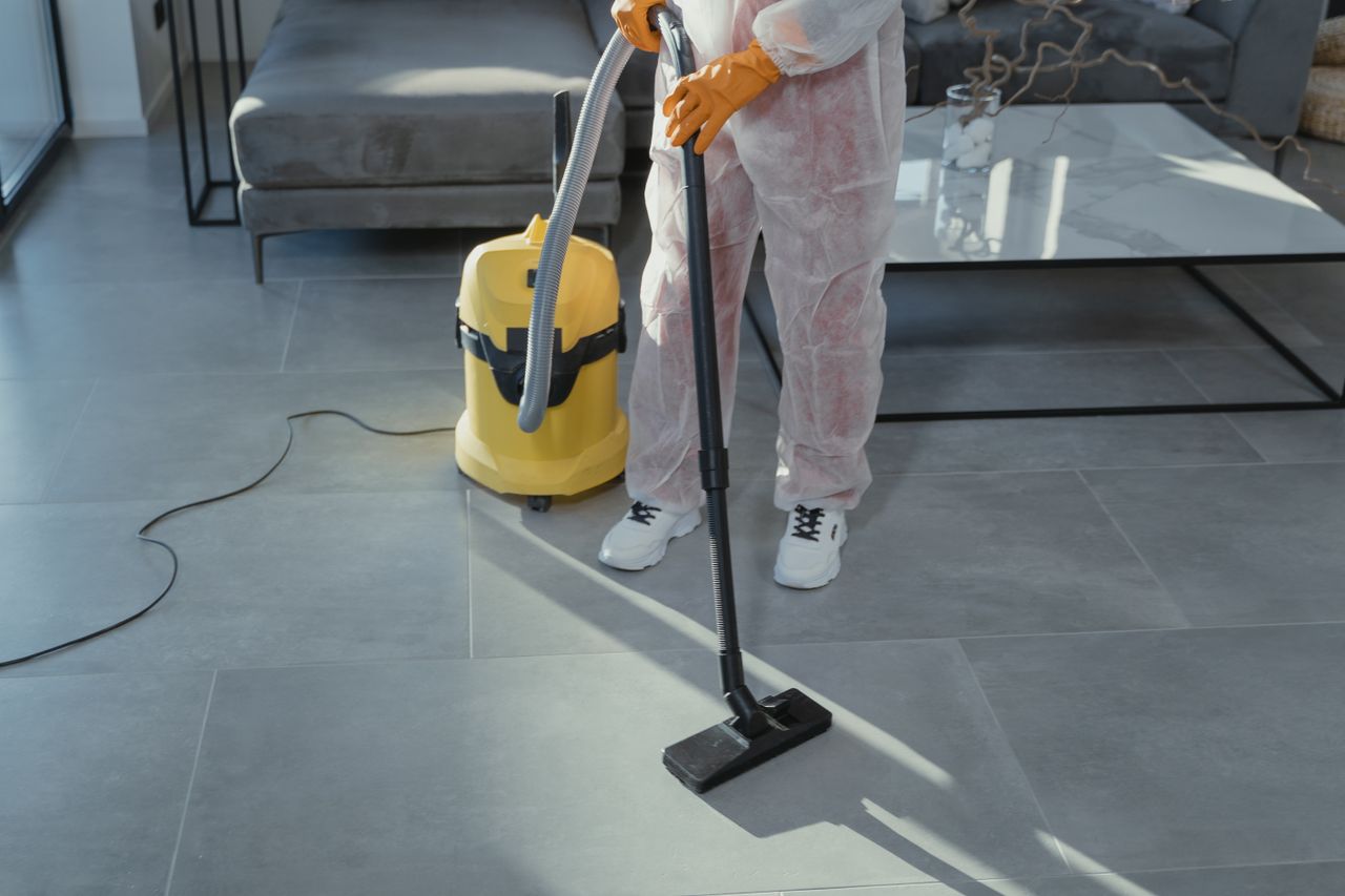 team-03 A professional cleaner in protective gear vacuuming the floor in a modern living room.